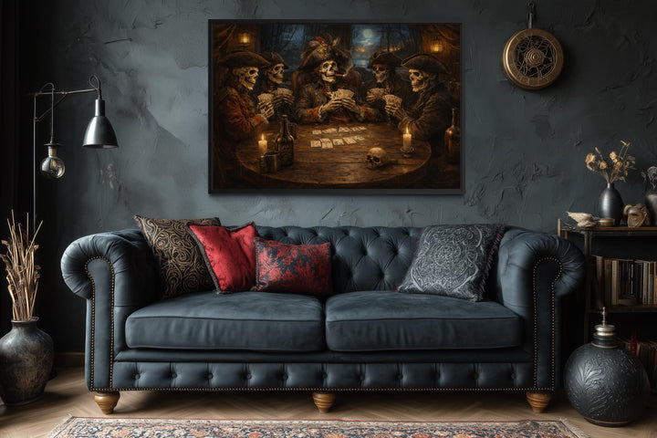 Framed wall art of skeleton pirates playing cards above a dark blue tufted sofa in a gothic room.