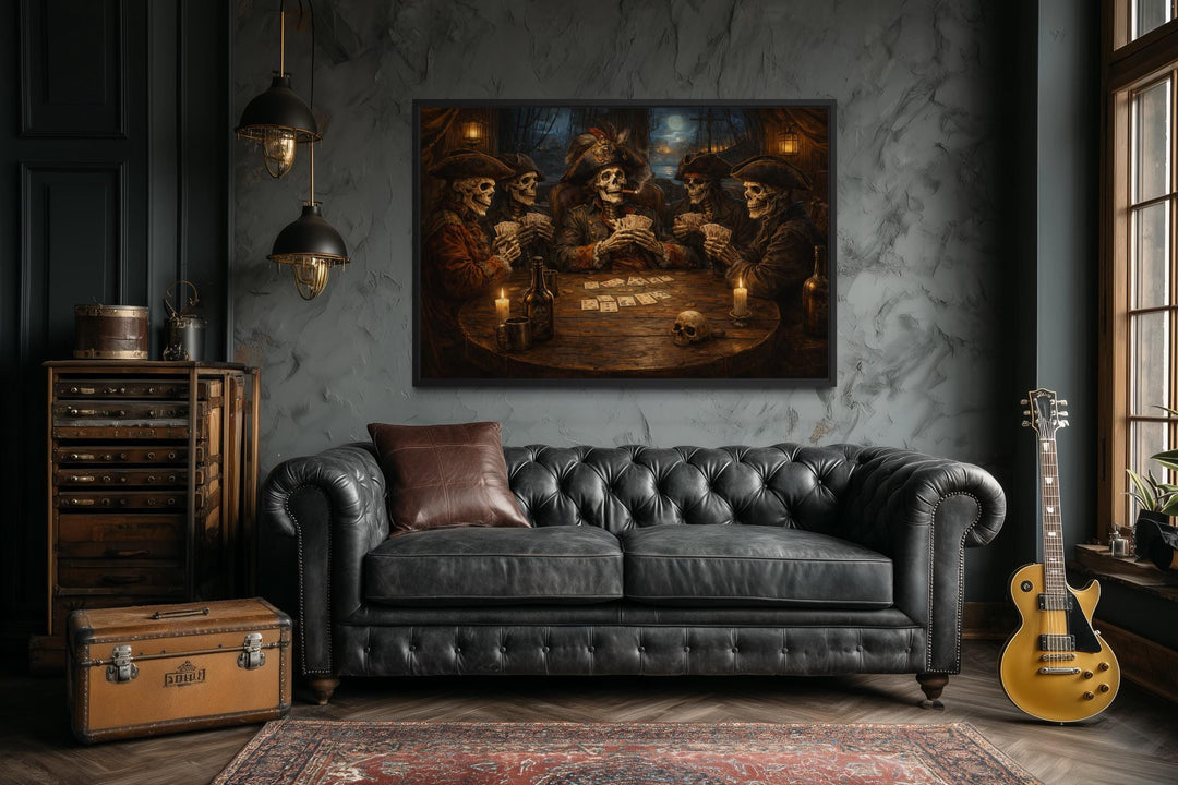A framed painting of skeleton pirates playing cards hangs above a black leather Chesterfield sofa.