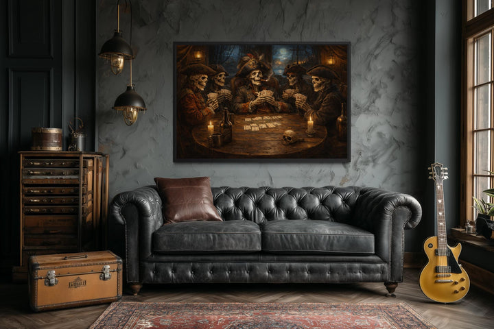 A framed painting of skeleton pirates playing cards hangs above a black leather Chesterfield sofa.