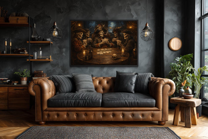 Framed wall art of skeleton pirates playing cards above a brown leather sofa in a gothic room.