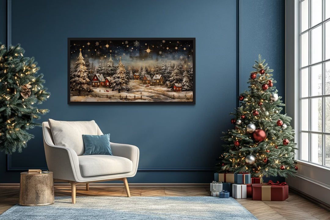 Snowy winter village at night wall art in a blue living room with a Christmas tree and armchair.