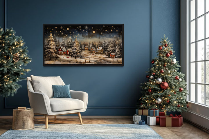 Snowy winter village at night wall art in a blue living room with a Christmas tree and armchair.