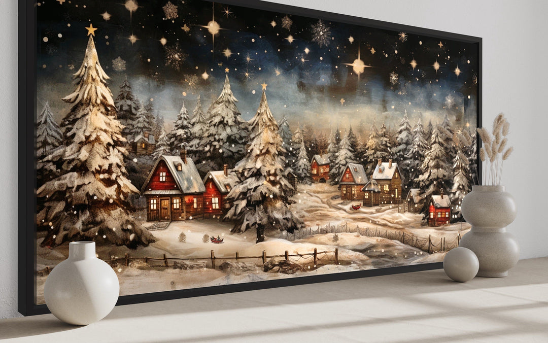Snowy winter village wall art with red cottages and starry night sky displayed on a mantel.