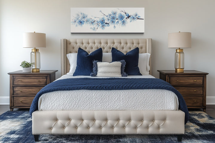 Soft blue blossom flowers long horizontal wall art hanging above a tufted bed in a bedroom.