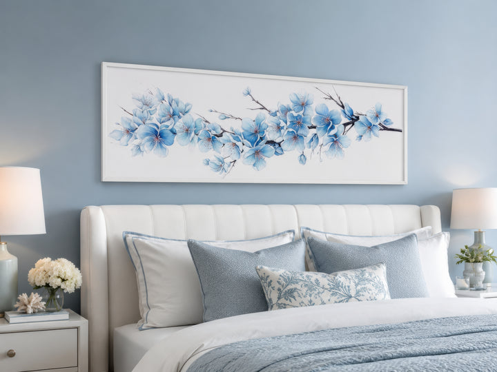 Long horizontal wall art of soft blue blossom flowers hanging above a white upholstered bed.