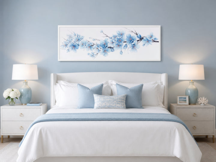 Soft blue blossom flowers long horizontal wall art hanging above a white bed in a blue bedroom.