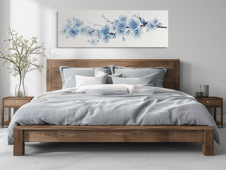 Soft blue blossom flowers long horizontal wall art hanging above a wooden bed in a bedroom.