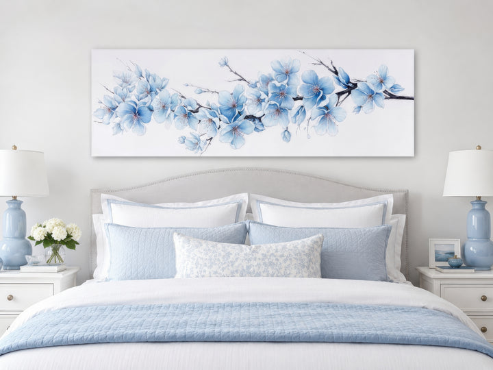 Long horizontal wall art of soft blue blossom flowers on a branch above a bed in a bedroom.