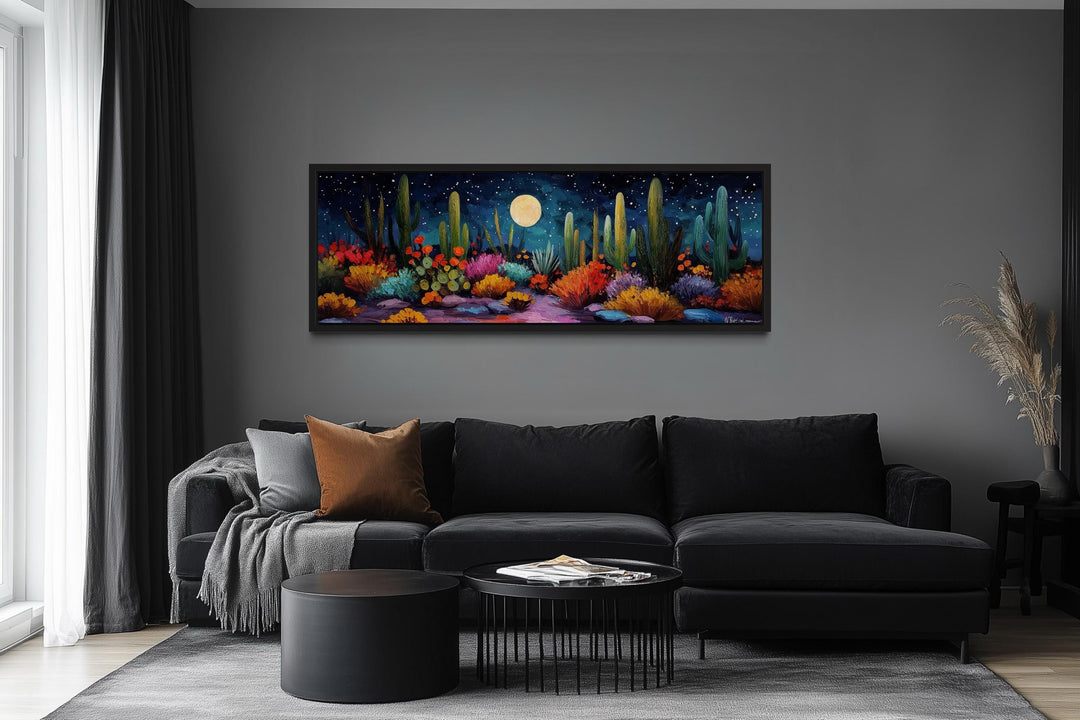 Southwest desert cacti under a moon and starry sky on a long horizontal canvas over a black sofa.
