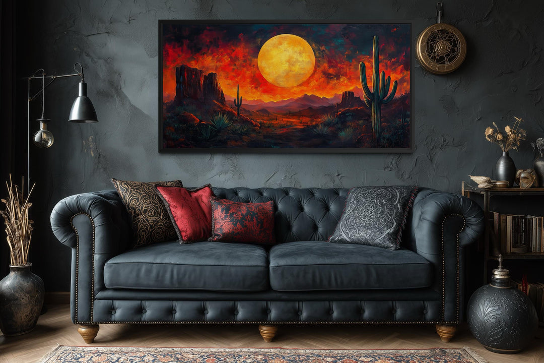 A dramatic red sunset canvas print with cactus silhouettes hangs above a dark tufted sofa.