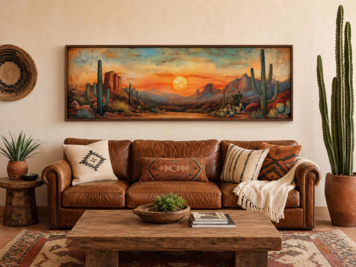 Panoramic Southwestern wall art of a desert sunset with saguaro cacti above a brown leather sofa.