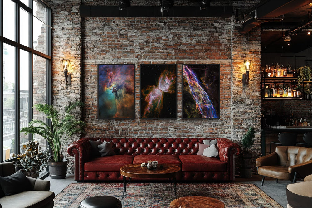 Three vertical space nebula canvas prints displayed above a red leather sofa in a brick loft.