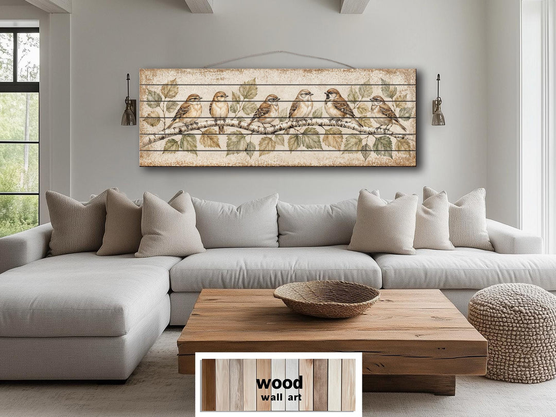 Sparrows on Birch Tree Branch distressed wood wall art hanging above a neutral sectional sofa.