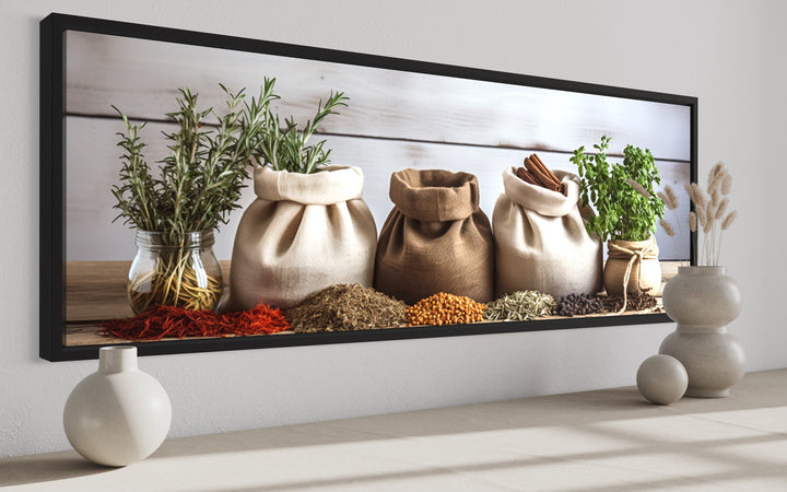 Framed horizontal wall art of rustic spice bags and fresh herbs on a kitchen counter.
