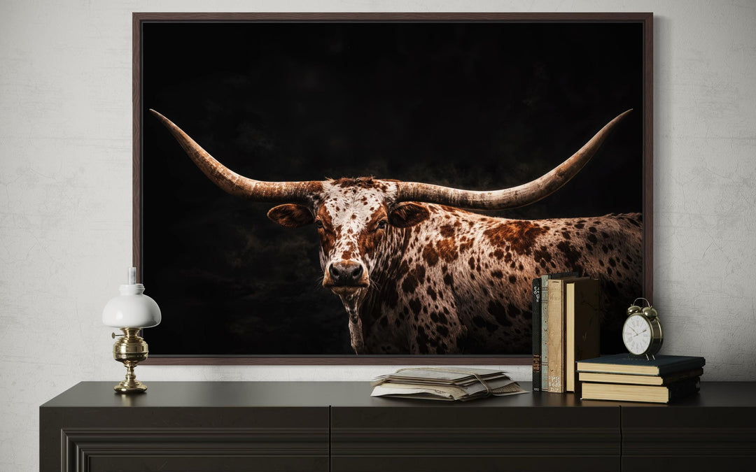 Spotted Texas Longhorn canvas print with a floating frame on a dark sideboard with rustic decor.