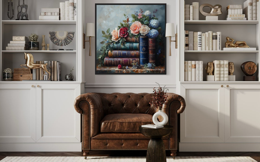 Framed canvas wall art of stacked books and flowers above a brown leather armchair in a library.