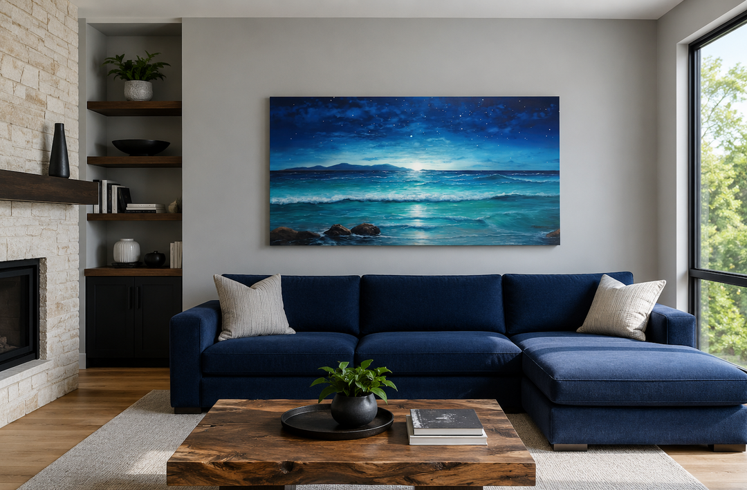 Panoramic framed canvas of a starry night sky over ocean waves hanging above a navy blue sofa.