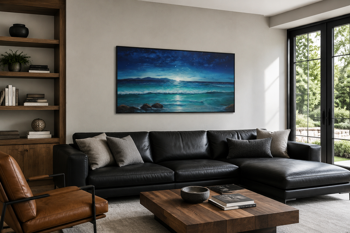Framed panoramic canvas art of a starry night over ocean waves hanging above a black leather sofa.