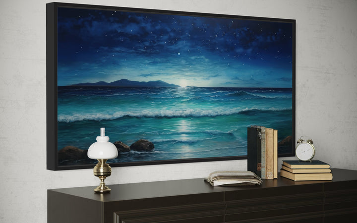 Framed panoramic canvas of a starry night over ocean waves, displayed above a dark wood console.