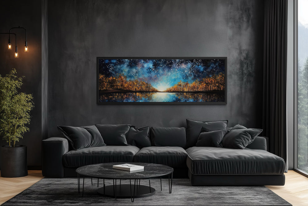 Starry sky over autumn forest and lake framed canvas wall art above a black sofa in a dark room.