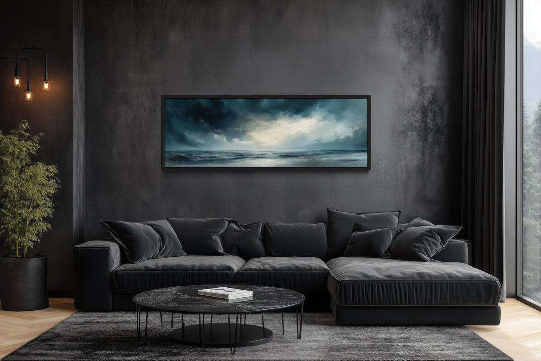 Panoramic canvas wall art of a stormy ocean horizon above a modern black sofa in a dark room.