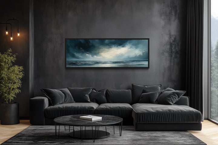 Panoramic canvas wall art of a stormy ocean horizon above a modern black sofa in a dark room.