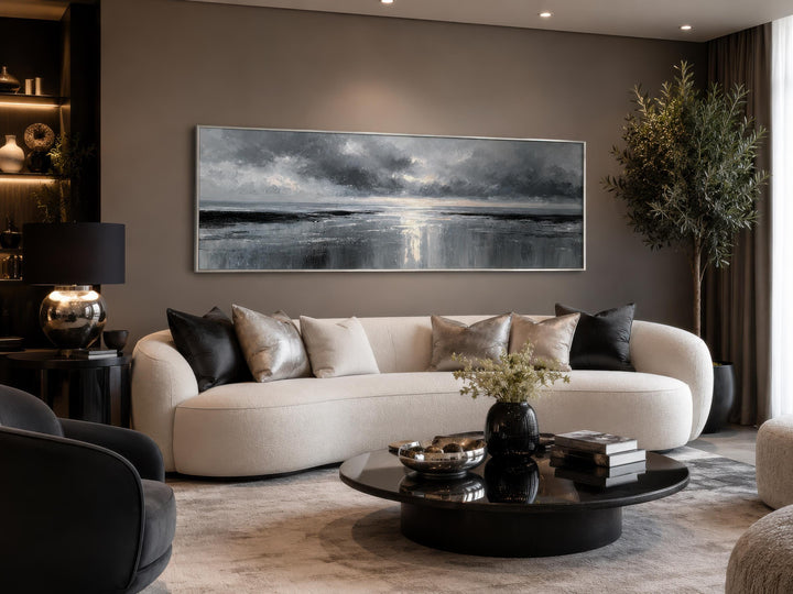 Long horizontal grey and silver canvas wall art of a stormy ocean above a modern white sofa.