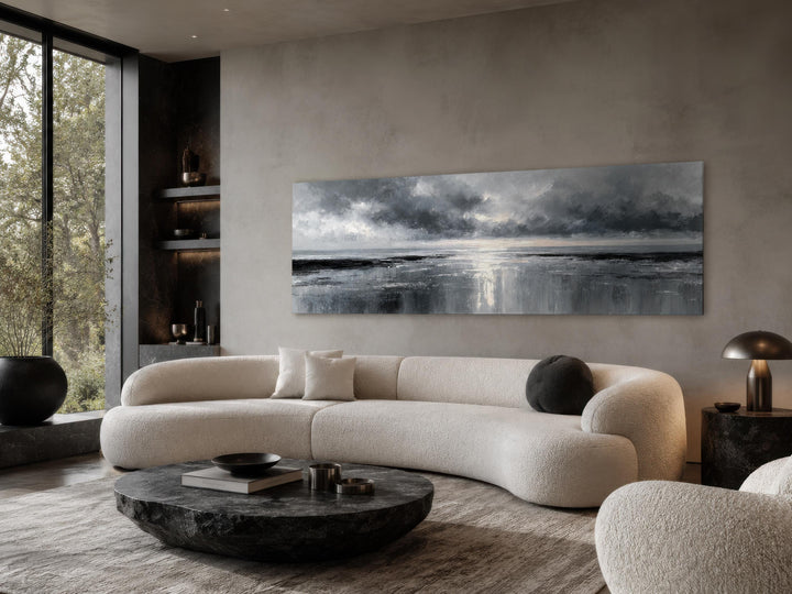 Long horizontal stormy ocean canvas art in grey and silver tones above a modern curved white sofa.