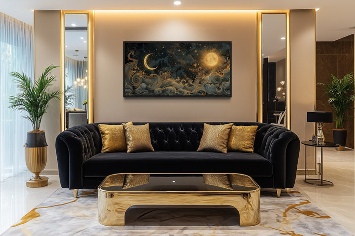 Framed black and gold celestial canvas art with sun and moon above a black sofa in a living room.