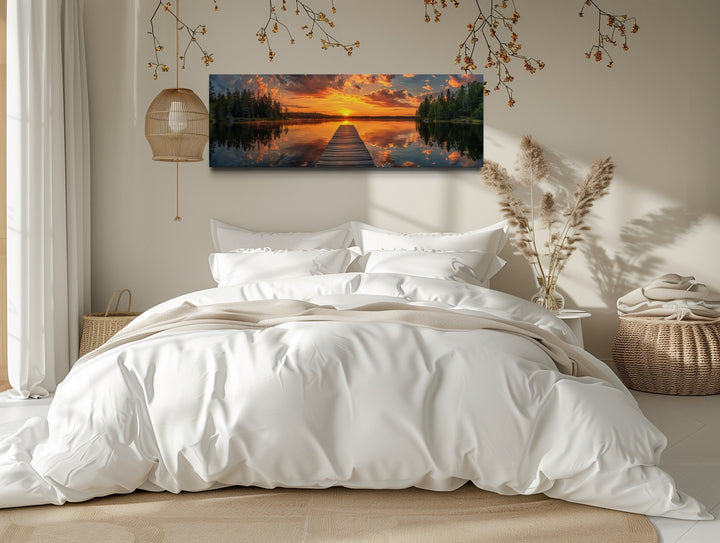 Sunrise over lake and fishing pier long horizontal canvas wall art hanging above a bed.