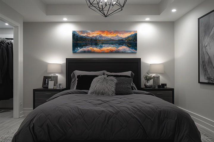 Panoramic framed canvas wall art of a sunset over a mountain lake hanging above a bed.