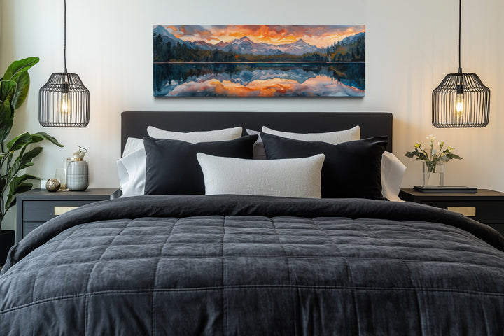 Panoramic framed canvas wall art of a sunset over a mountain lake hanging above a bed.