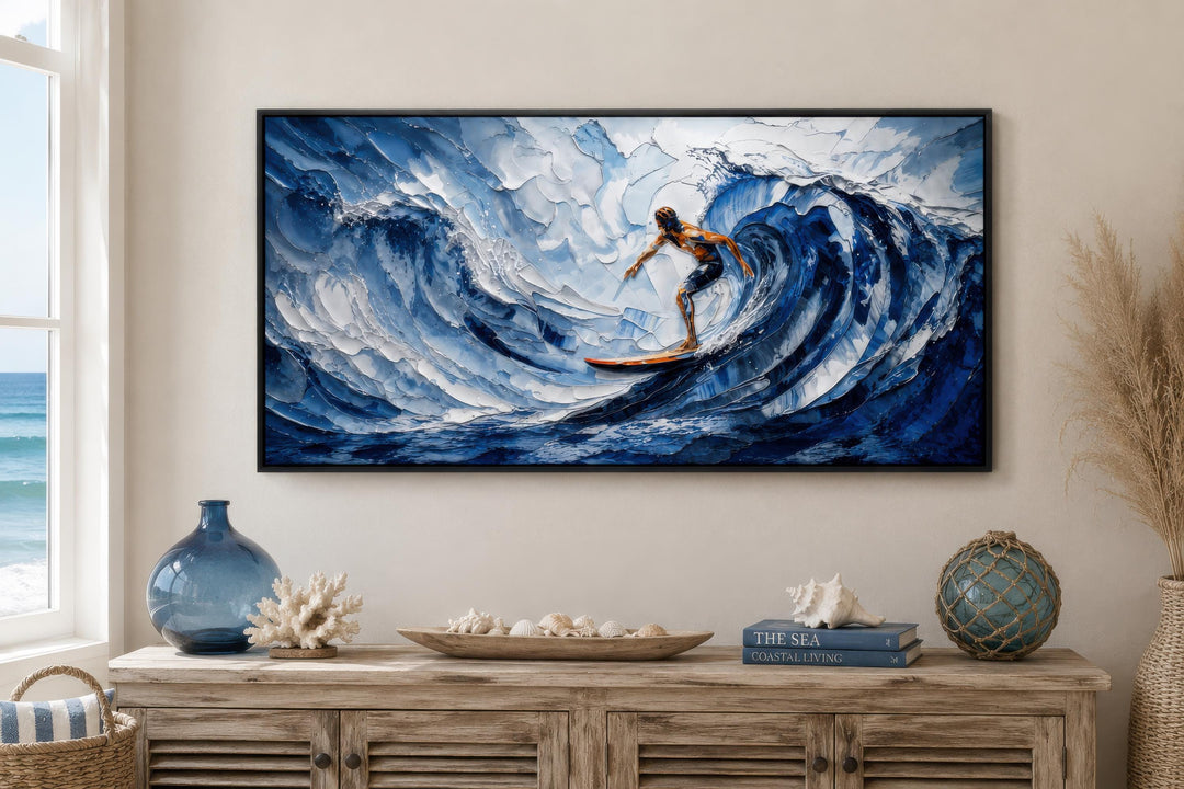 A horizontal canvas print of a surfer on a textured blue wave hangs above a coastal-style console.