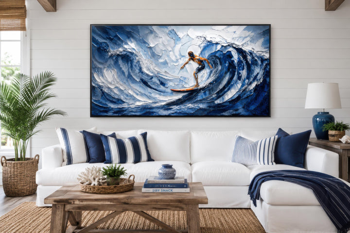 A large canvas print of a surfer on a blue ocean wave hangs above a white sofa in a coastal room.