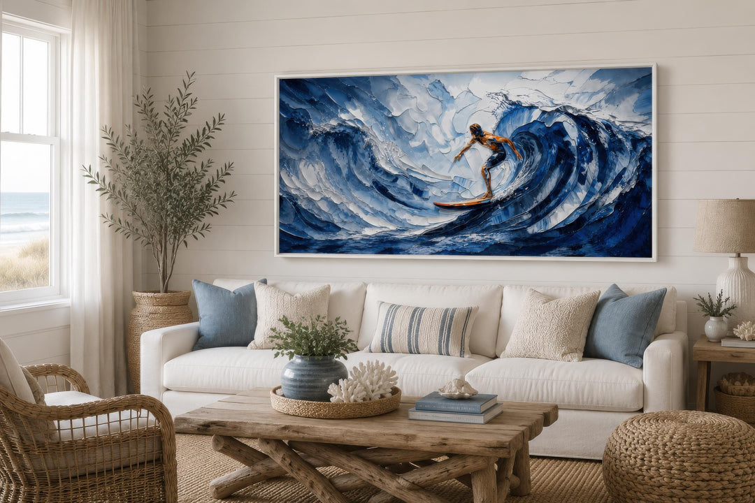 A large horizontal canvas print of a surfer on a blue wave in a coastal living room.