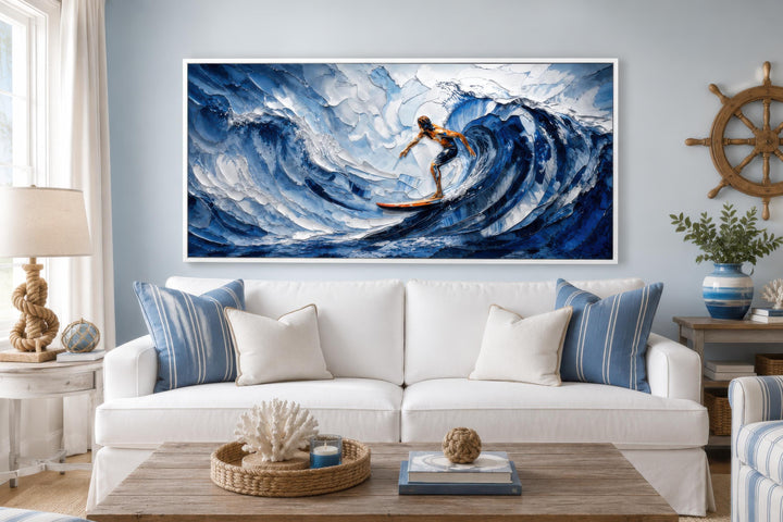 A wide horizontal canvas print of a surfer on a large blue wave in a coastal living room.