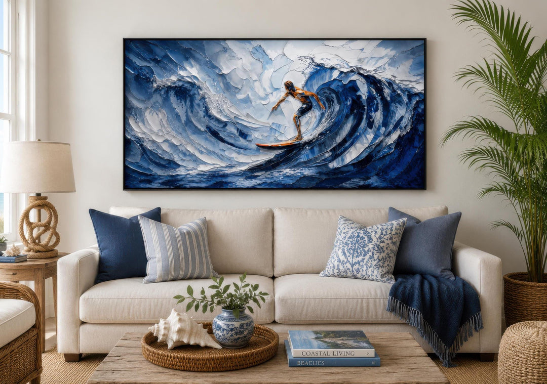 A large horizontal canvas print of a surfer on a blue wave hangs above a white sofa in a beach house.