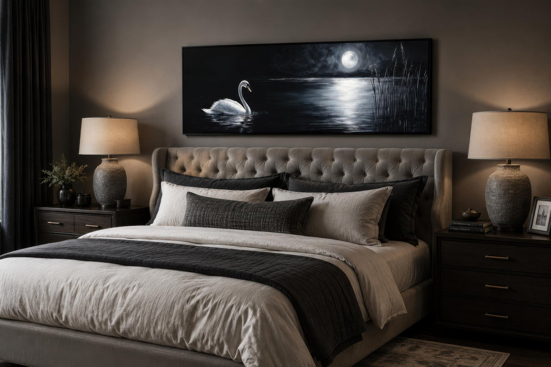 Long narrow canvas print of a white swan on a moonlit lake above a bed in a dark moody bedroom.
