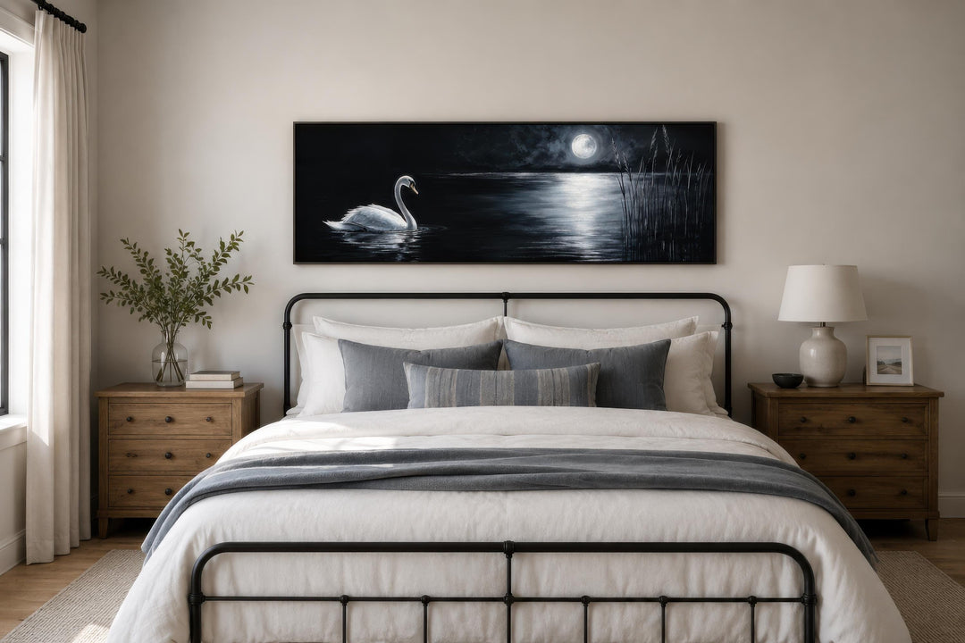 Long narrow canvas print of a white swan on a moonlit lake, hung above a bed in a moody bedroom.