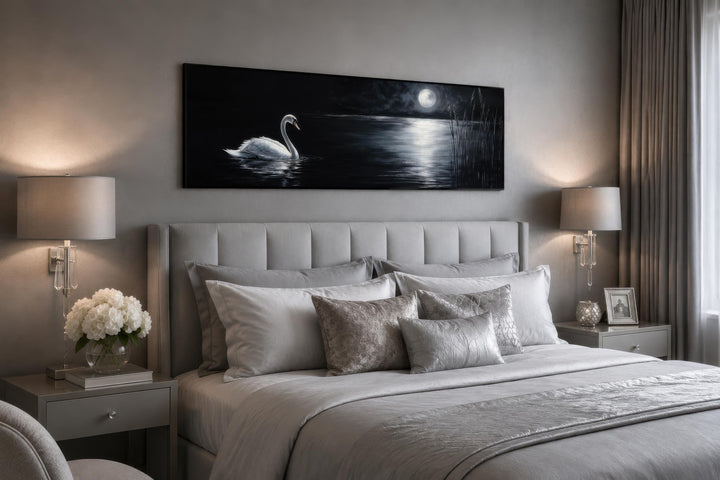 Long narrow canvas print of a white swan on a moonlit lake hanging above a grey upholstered bed.
