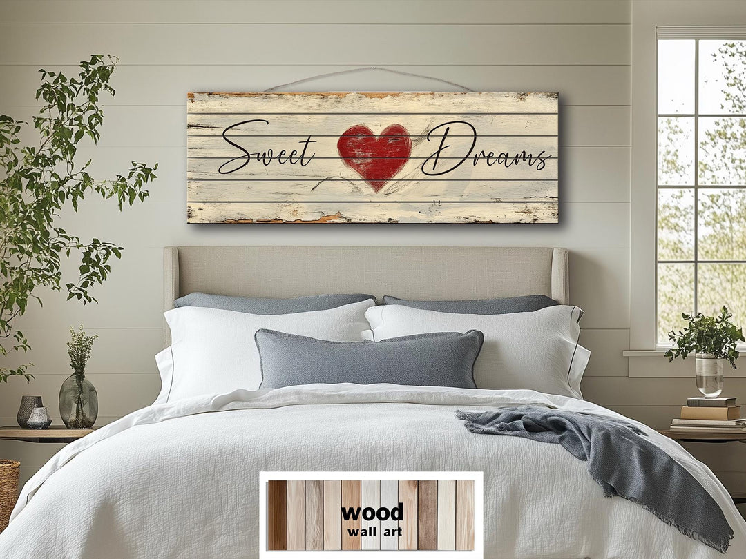 A long horizontal rustic wood sign with Sweet Dreams and a red heart hangs above a bed.