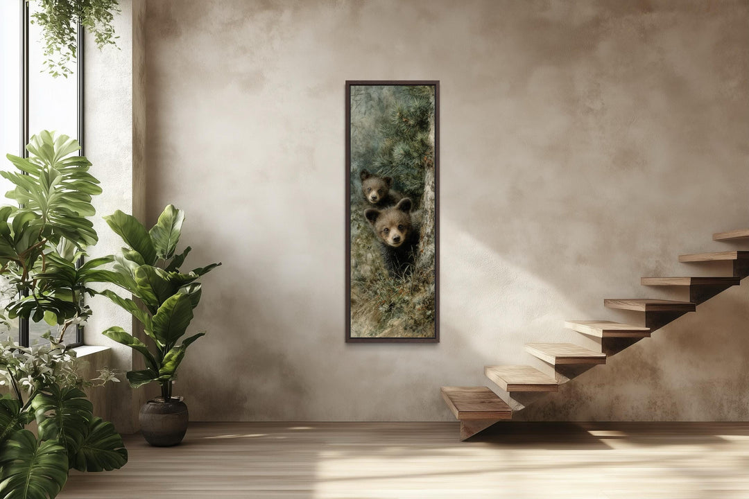 Tall narrow canvas wall art of two baby bear cubs peeking from a pine tree in a rustic room.