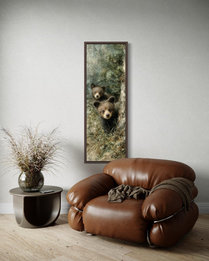 Tall narrow canvas wall art featuring two baby bear cubs peeking from a pine tree in a cabin setting.