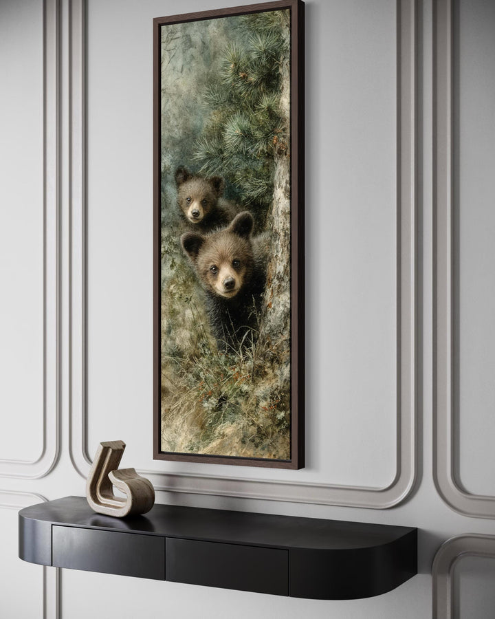 Tall narrow canvas wall art of two baby bear cubs peeking from a pine tree in a modern room.