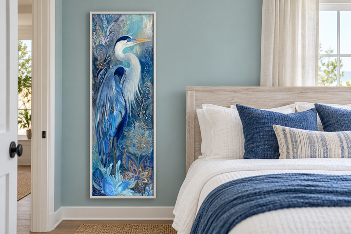 Tall narrow canvas print of a blue heron in a white frame, hanging in a coastal style bedroom.