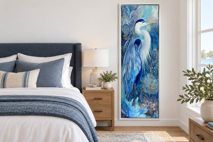 Tall narrow canvas print of a blue heron in a white frame, hanging in a modern coastal bedroom.