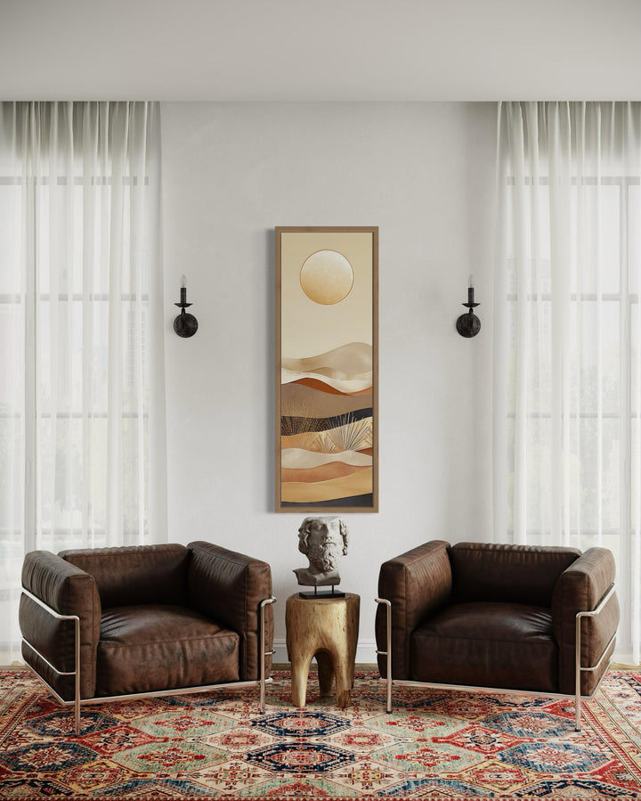 Tall narrow boho canvas art featuring a sun over desert dunes in earthy tones on a white wall.