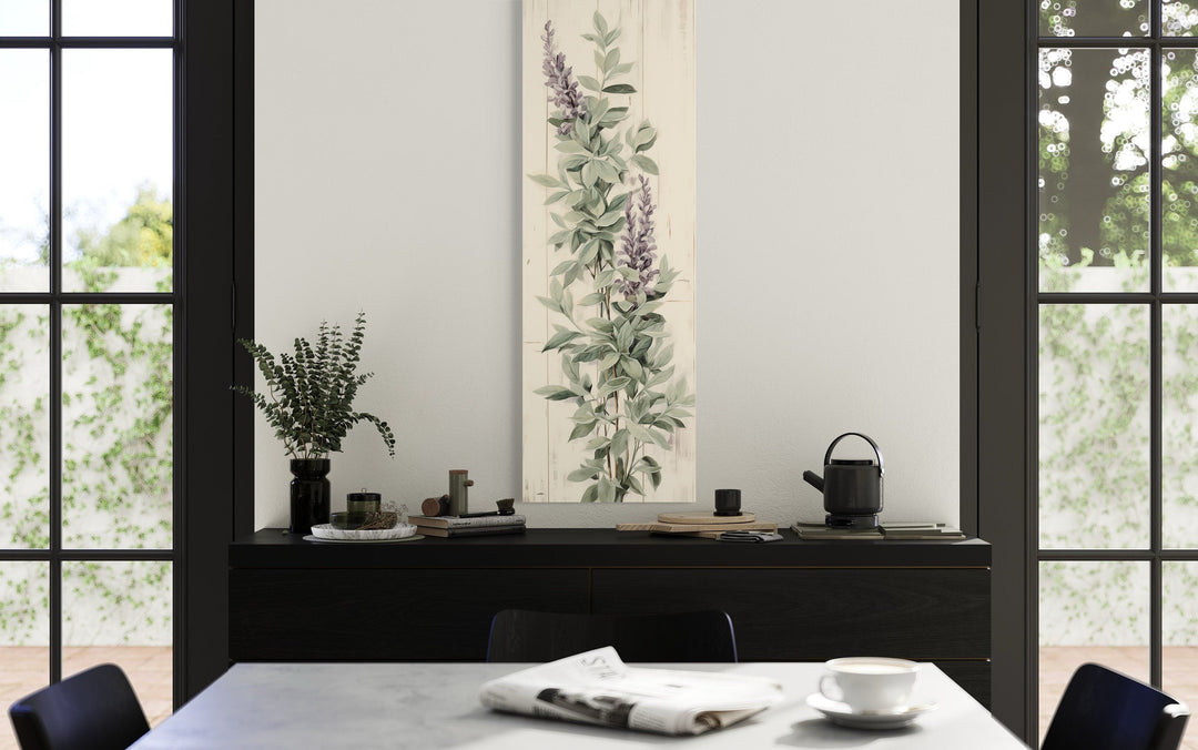 Vertical framed canvas wall art featuring sage green basil leaves and purple flowers on a wall.