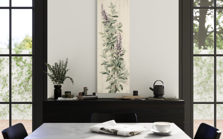 Vertical framed canvas wall art featuring sage green basil leaves and purple flowers on a wall.
