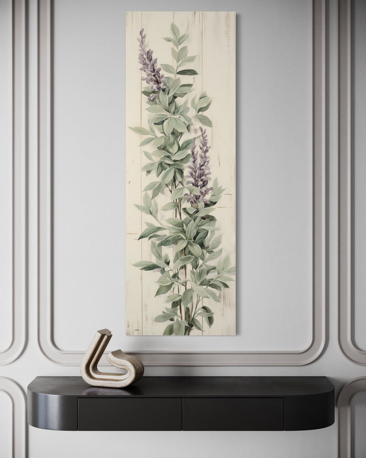 Vertical framed canvas wall art featuring sage green basil leaves and purple flowers on a wall.